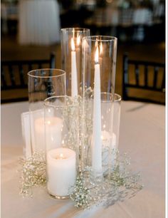 candles and flowers on a table in a room with white linens, chairs and tables