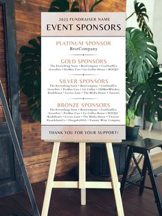 an event sponsor sign in front of a wooden paneled wall with potted plants