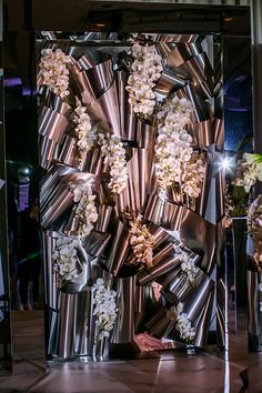 an art installation made out of metal pipes with flowers on the side and lights behind it