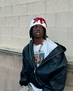 a man wearing a hat and jacket leaning against a wall with his hands in his pockets