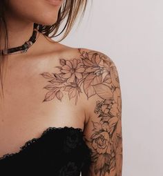 a woman wearing a black dress with flowers on her chest and arm tattooing it's upper half