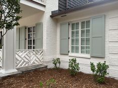 a white brick house with green shutters and trees in front of the window area