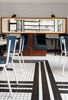 an empty restaurant with blue chairs and white tablecloths on the floor, in front of a large mirror