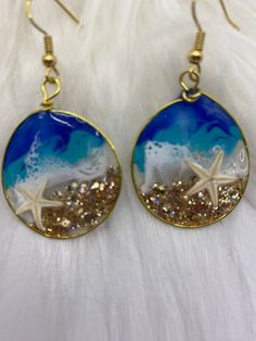 *These are unique handmade earrings. The earrings you receive will be similar to the ones pictured; however, the blue tone and wave styles will vary* Beautiful handmade earrings inspired by the beautiful coast of North Carolina.  Each set has hand shaped gold tone wired hoops and are decorated with gold glitter, resin, mica powder (which adds a hint of shimmer) and a real starfish.  You or your loved one will have a truly one-of-a kind handmade pair of earrings. Great addition to your tropical state-of-mind jewelry accessory collection. Specifications:  Gold wire Made with epoxy resin *These handcrafted earrings may have small imperfections* Blue Hoop Earrings With Ear Wire For Beach, Handmade Adjustable Ocean-inspired Earrings, Gold Ocean-inspired Beach Earrings, Handmade Ocean-inspired Gold Earrings, Unique Gold Earrings For Beach, Nickel Free Ocean-inspired Gold Earrings, Ocean-inspired Blue Earrings With Ear Wire, Nickel Free Gold Ocean-inspired Earrings, Ocean-inspired Gold Wire Wrapped Jewelry