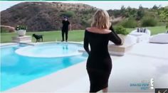 a woman in a black dress standing next to a pool with a dog on the other side