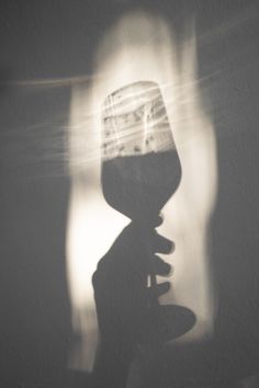 the shadow of a person holding a wine glass in front of a wall with light coming through it