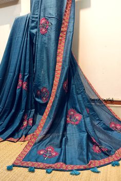 This blue handloom soft cotton saree is a true embodiment of style meeting comfort. With its beautiful floral motif embroidery, neatly done, and the addition of a printed border and tassels, it becomes a captivating and unique piece. The inclusion of both a running blouse piece and a matching cotton printed blouse piece adds further flexibility, allowing you to showcase your style effortlessly in any occasion. Details: Blouse: Yes. With matching printed cotton Blouse Piece Fabric: Handloom soft cotton saree Work: Machine Embroidery work [* This work is neither Computerized Machine Embroidery work nor machine Aari Embroidery with woolen thread. * It's completely Manual Machine Embroidery Work with silk threads..] Saree length:  6.3 mtrs Saree width: 45 inches Fall & Picot: You do not need a Cotton Traditional Wear With Printed Border, Blue Cotton Traditional Wear With Embroidered Border, Bohemian Cotton Saree With Multicolor Embroidery, Multicolor Embroidered Cotton Saree For Diwali, Cotton Saree With Multicolor Embroidery For Diwali, Blue Cotton Traditional Wear With Printed Border, Traditional Cotton Saree With Resham Embroidery, Embroidered Cotton Saree For Festive Season, Embroidered Mulmul Saree For Diwali