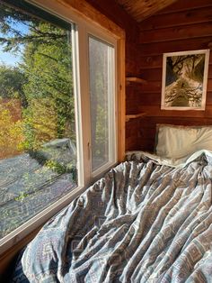 a bed in a bedroom next to a window with a view of the woods outside