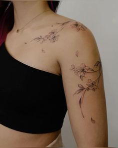 a woman wearing a black top with flowers on her chest and arm tattooing it