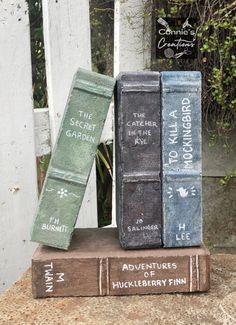 three books stacked on top of each other in front of a white picket fence and bushes