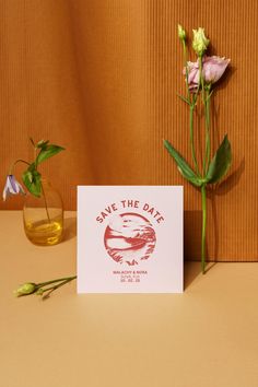 two flowers are sitting next to a card with the save the date logo on it