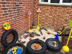 there are many toy cars and tires in front of a building with rocks, gravel, and sand