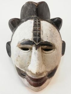 a white mask with black and brown designs on it's face, against a white background