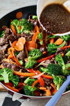 stir fry with beef, broccoli and carrots in a pan next to a spatula