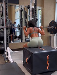 a woman is squatting on a bench in the gym while holding a barbell