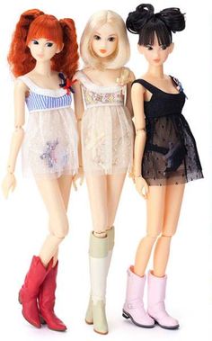 three dolls standing next to each other in front of a white background and one has red hair