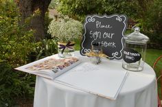 a table topped with a menu and jars filled with flowers next to a sign that says please, stop our cookbook