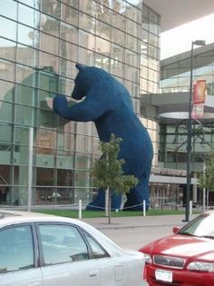 there is a giant blue bear on the side of a building next to two cars