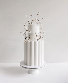 a three tiered white cake with daisies on the top and bottom, in front of a plain background