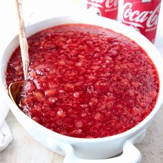 a white bowl filled with red liquid next to two coca cola cans