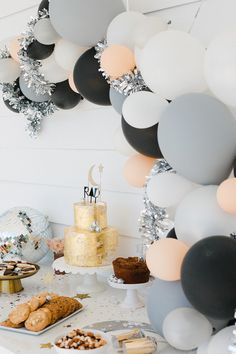 a table topped with cake and balloons next to a wall filled with confetti