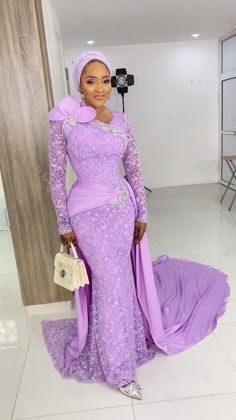 a woman wearing a purple gown and holding a white purse standing in front of a wall