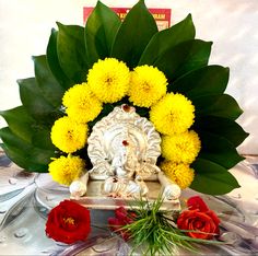 an arrangement of yellow and red flowers in front of a small gan idol with green leaves