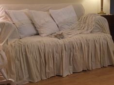 a couch covered in white ruffled linens with pillows and blankets on the back