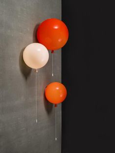 two orange and white balloons hanging on the wall next to each other in front of a gray wall