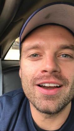 a man wearing a hat is smiling for the camera while sitting in a car with his eyes wide open