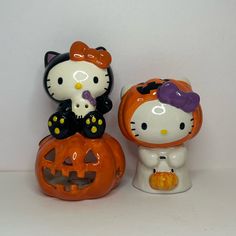 two hello kitty figurines sitting next to each other on top of a pumpkin