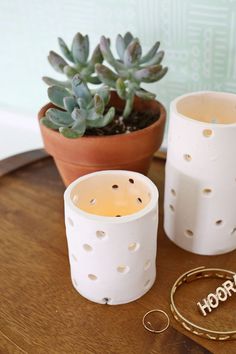 two white candles sitting on top of a wooden table next to a potted plant