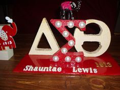 a red and white sign with pearls on it sitting on a wooden table next to two small figurines