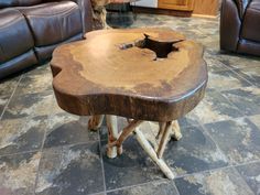 a wooden table sitting on top of a tile floor next to leather couches in a living room