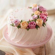 a white cake with pink frosting and flowers on top sitting on a wooden table