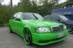 a green car parked next to other cars in a parking lot