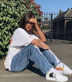 a woman sitting on the ground with her hands in her hair and wearing white sneakers