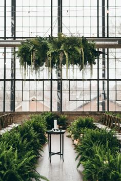 an indoor wedding ceremony with greenery and candles on the tables in front of large windows