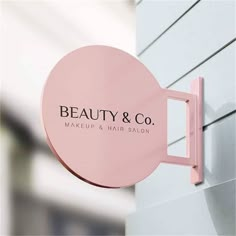 a pink sign hanging on the side of a building that says beauty & co makeup and hair salon