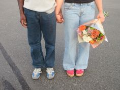 two people holding hands while standing next to each other with flowers in their lap and shoes on