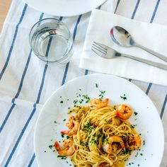 a plate of pasta with shrimp and parsley on the side next to a glass of water