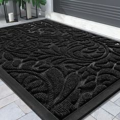 a large black door mat on the ground in front of a doorway with a plant