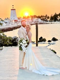 a bride and groom standing on a dock at sunset