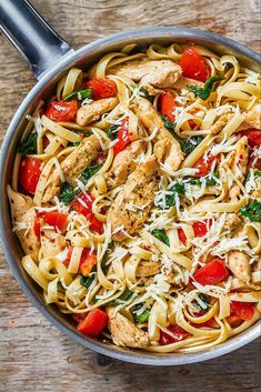 a skillet filled with chicken, tomato and spinach noodle dish on top of a wooden table