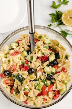 a pasta salad in a glass bowl with a serving utensil on the side