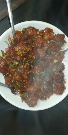 a white plate topped with meat and vegetables on top of a black table next to a fork