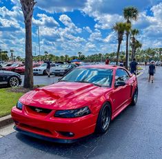 a red car parked on the side of a road next to palm trees and people