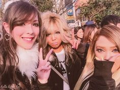 two women making the peace sign with their fingers in front of them and people behind them