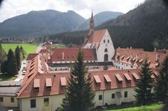 an aerial view of a large building in the middle of trees and mountains behind it