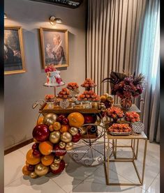 a table with oranges and apples on it in front of a painting hanging on the wall